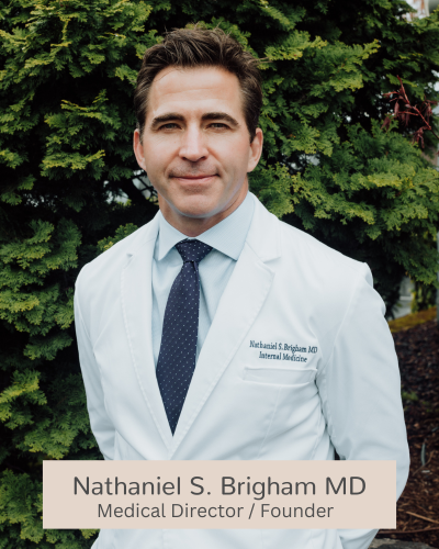 This picture illustrates a staff headshot of Dr. nathaniel Brigham of Aluma Aesthetic Medicine in Portland, OR. He has his white lab coat on and is smiling. 